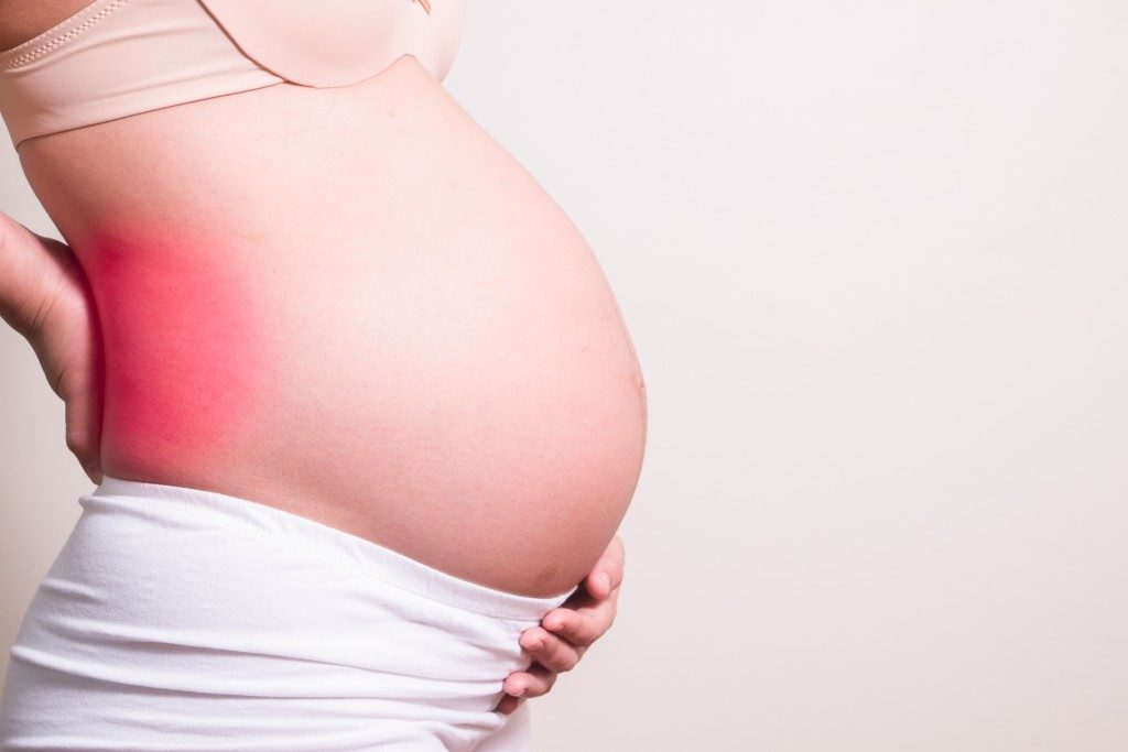 Pregnant woman with a strong pain massaging her backache - pain in red
